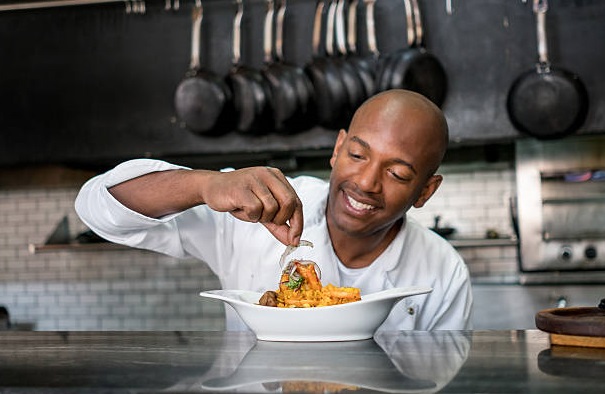 African American chef decorating a plate and working at a restaurant -  food and drinks concepts